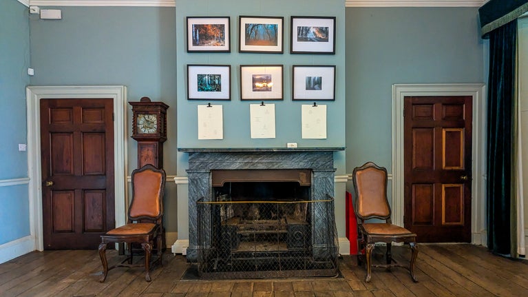 View of framed photographs hanging on the walls in the Terrace Room. The Terrace room has varnished wood floorboards and teal coloured walls.
